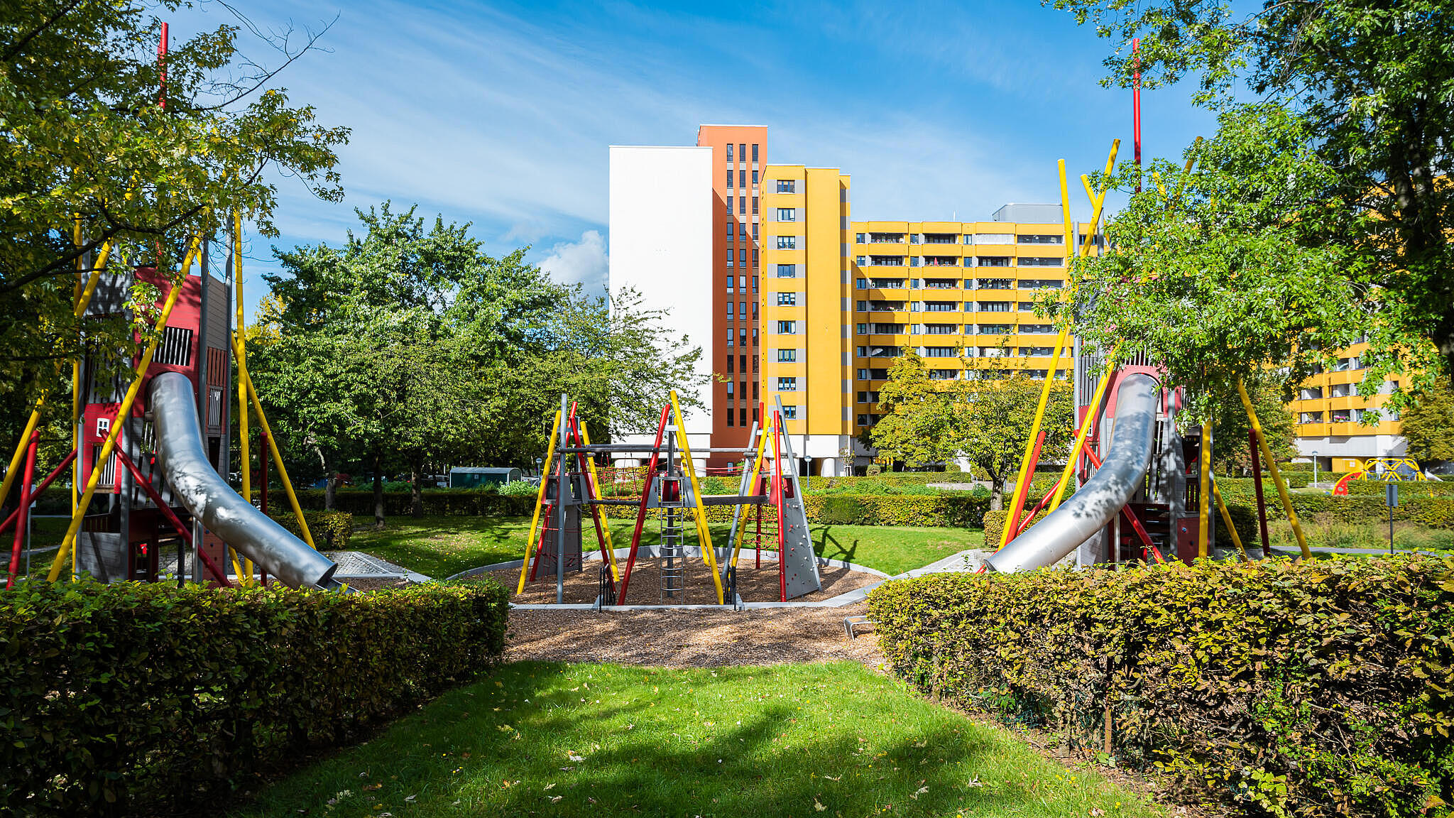Bild zeigt neugestaltete Grünanlagen und Spielgerüst mit Rutschen. Im Hintergrund Bäume und Wohnhaus.