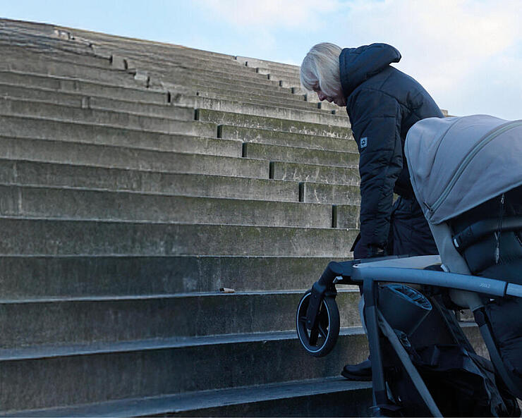 Zwei Personen tragen einen Kinderwagen eine Treppe hinauf