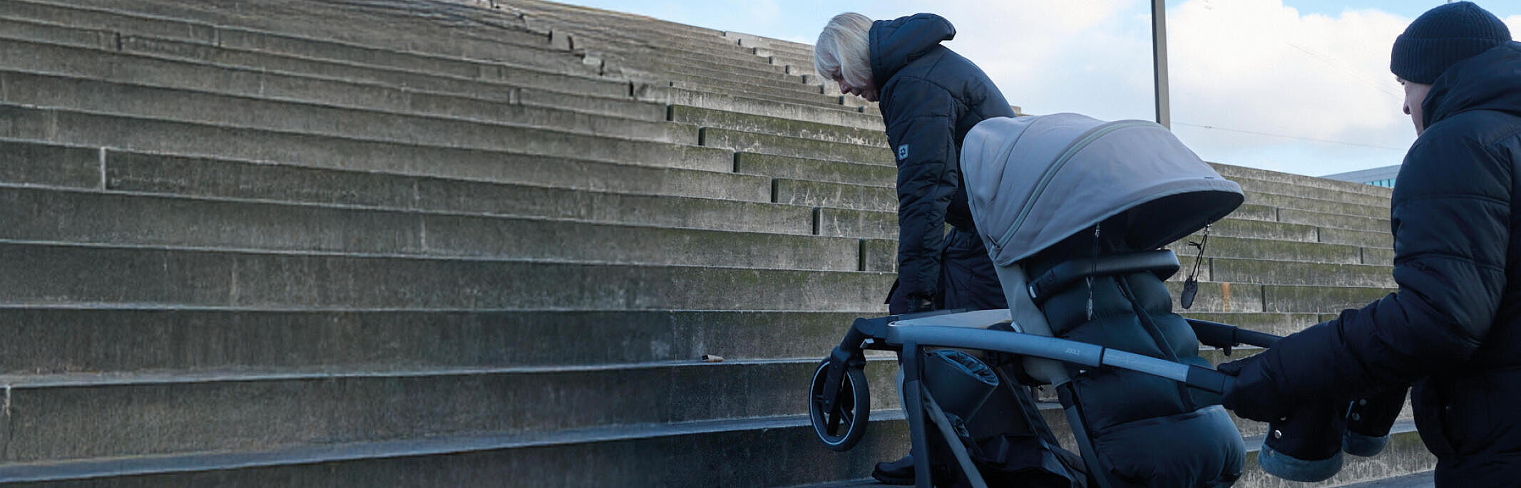 Zwei Personen tragen einen Kinderwagen eine Treppe hinauf