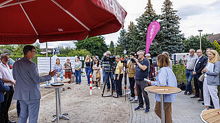 Foto zeigt Gäste bei der Schlüsselübergabe. Sie hören den Redebeiträgen zu.