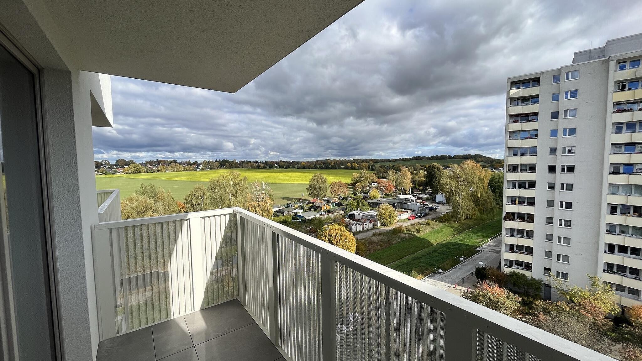 Außenaufnahme zeigt die Sicht aus einem der Balkone des Neubaus Finsterwalder Straße - ein grünes Feld im Sonnenschein, das hinter der Stadtgrenze in Brandenburg liegt. 