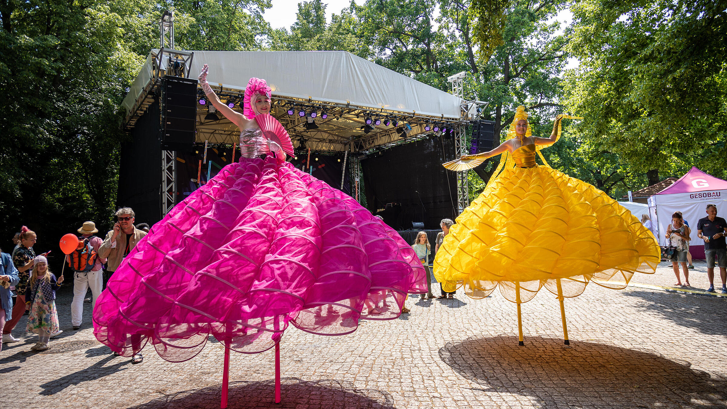 Außenaufnahme zeigt die beiden Stelzenläuferinnen in Gelb und Pink.