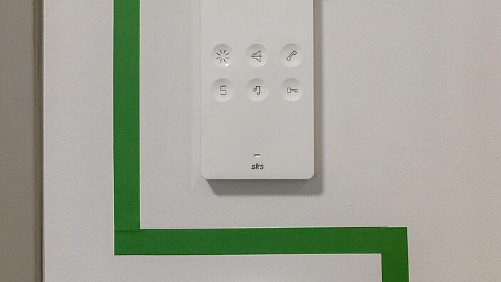 Technische Geräte sind an einer Wand befestigt. Zu sehen ist ein Bewegungssensor und Türklingelverstärker.