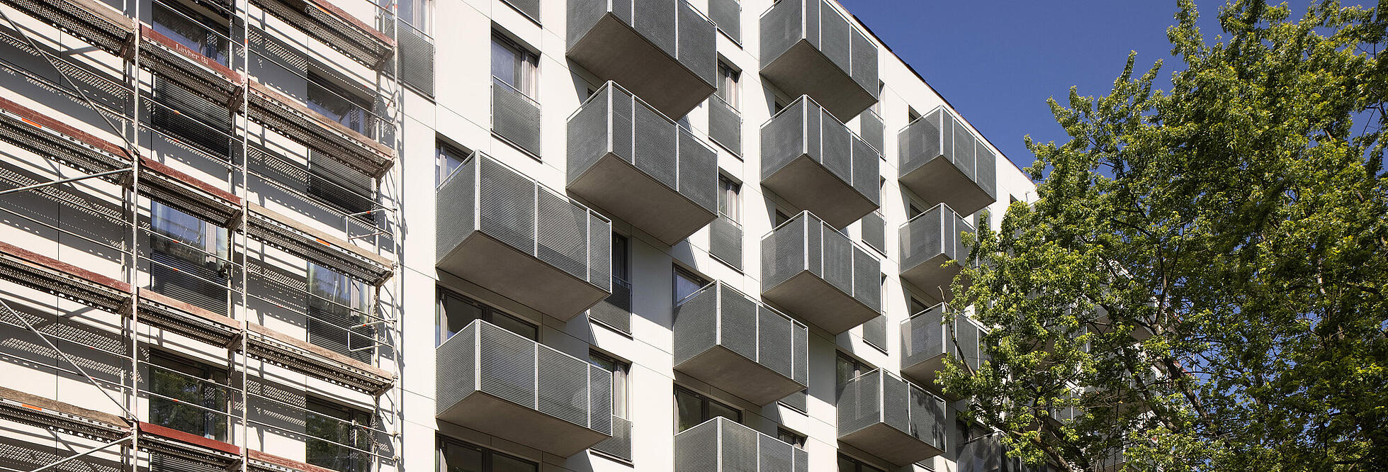 Außenaufnahme zeigt die teilweise abgerüstete Fassade in der Armenischen Straße. Rechter Hand gut erkennbar die grauen Balkone, die sich gut von der weißen Fassade abheben.  