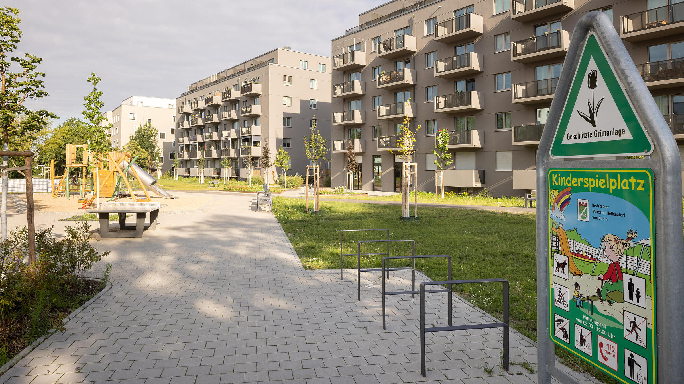 Eingang zu grünen Stadtpark mit zwei mehrstöckigen modernen Wohnhäusern im Hintergrund.