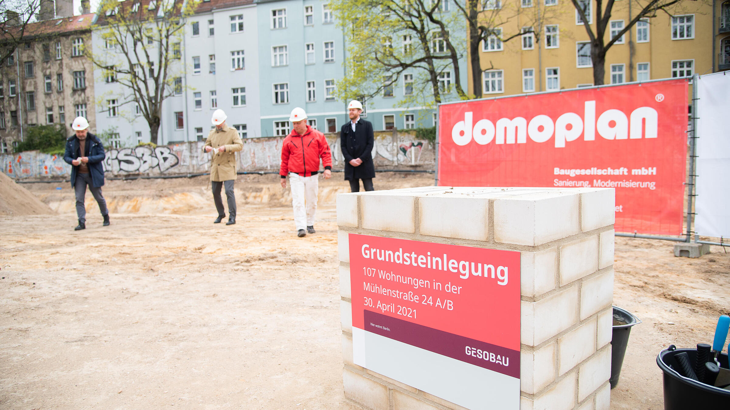 Rechts im Vordergrund der fertige Grundstein, im Hintergrund vier Personen