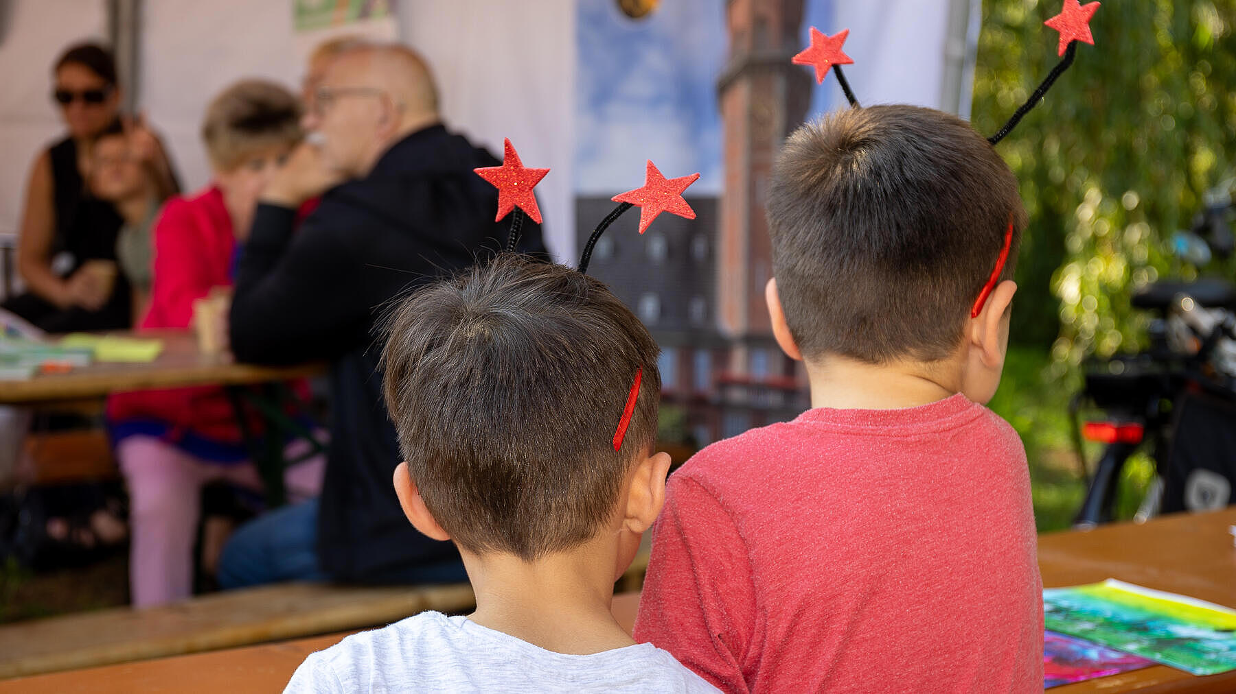 Außenaufnahme zeigt zwei Kinder mit dem Rücken zur Kamera. Beide tragen einen Kopfschmuck aus Sternen an Fühlern.