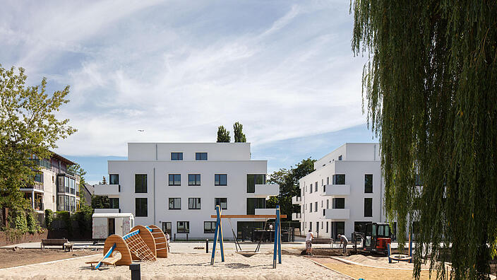 Weitwinkelaufnahme außen: Im Vordergrund ein Spielplatz mit Wipptieren, im Hintergrund in der Bildmitte zwei neu gebaute Häuser in der Abajstraße / Kastanienallee.