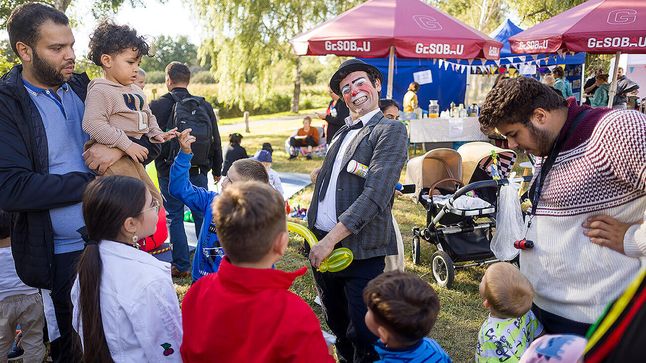 Ein Clown schneidet, umringt von vielen Kindern unterschiedlichen Alters, Grimassen.