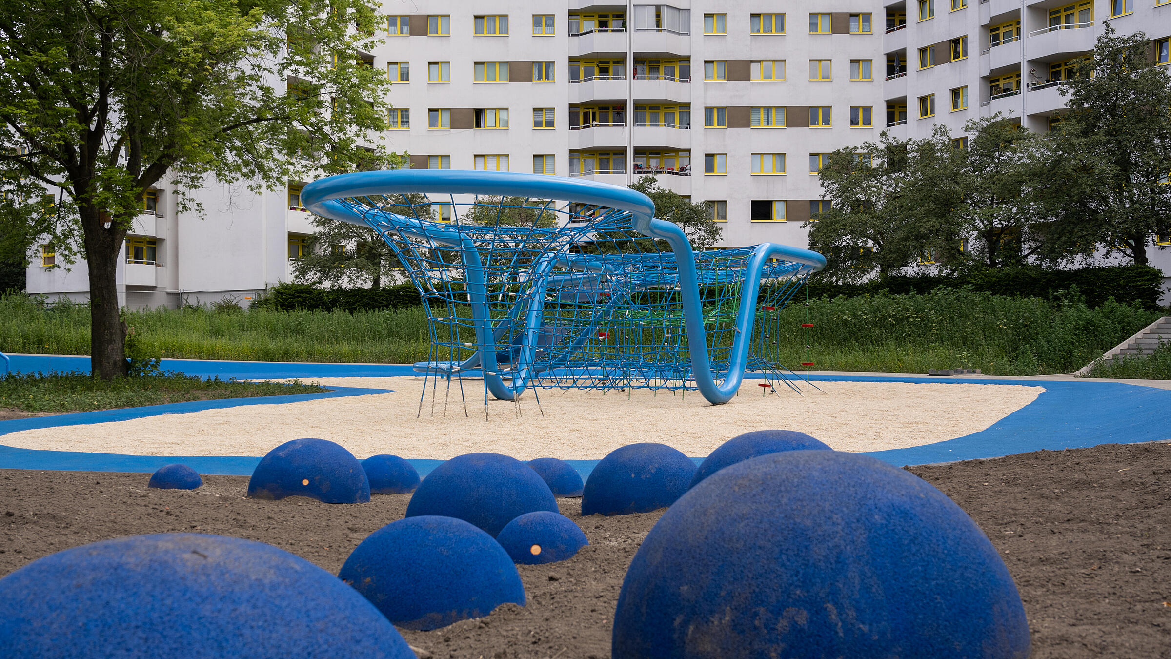 Außenaufnahme zeigt Detail des blauen Balancierpfads in der "Wasserschlucht". Im Hintergrund ein Mehrfamilienhaus der Quickborner Straße.