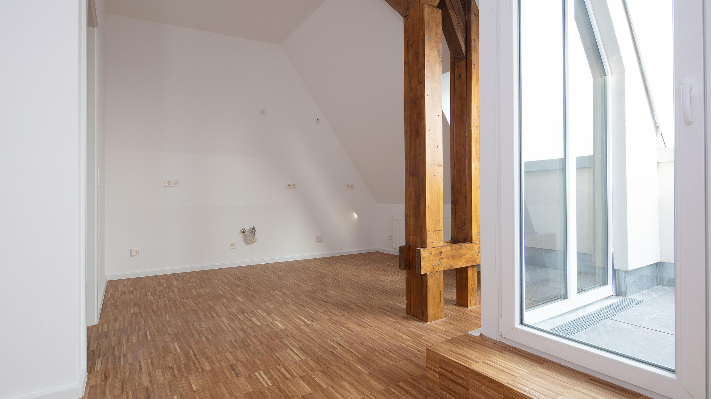 Innenaufnahme zeigt eine frisch gebaute Dachgeschosswohnung in der Luxemburger Straße. Rechter Hand ist der Zugang zu einem Balkon via Glastür sichtbar.