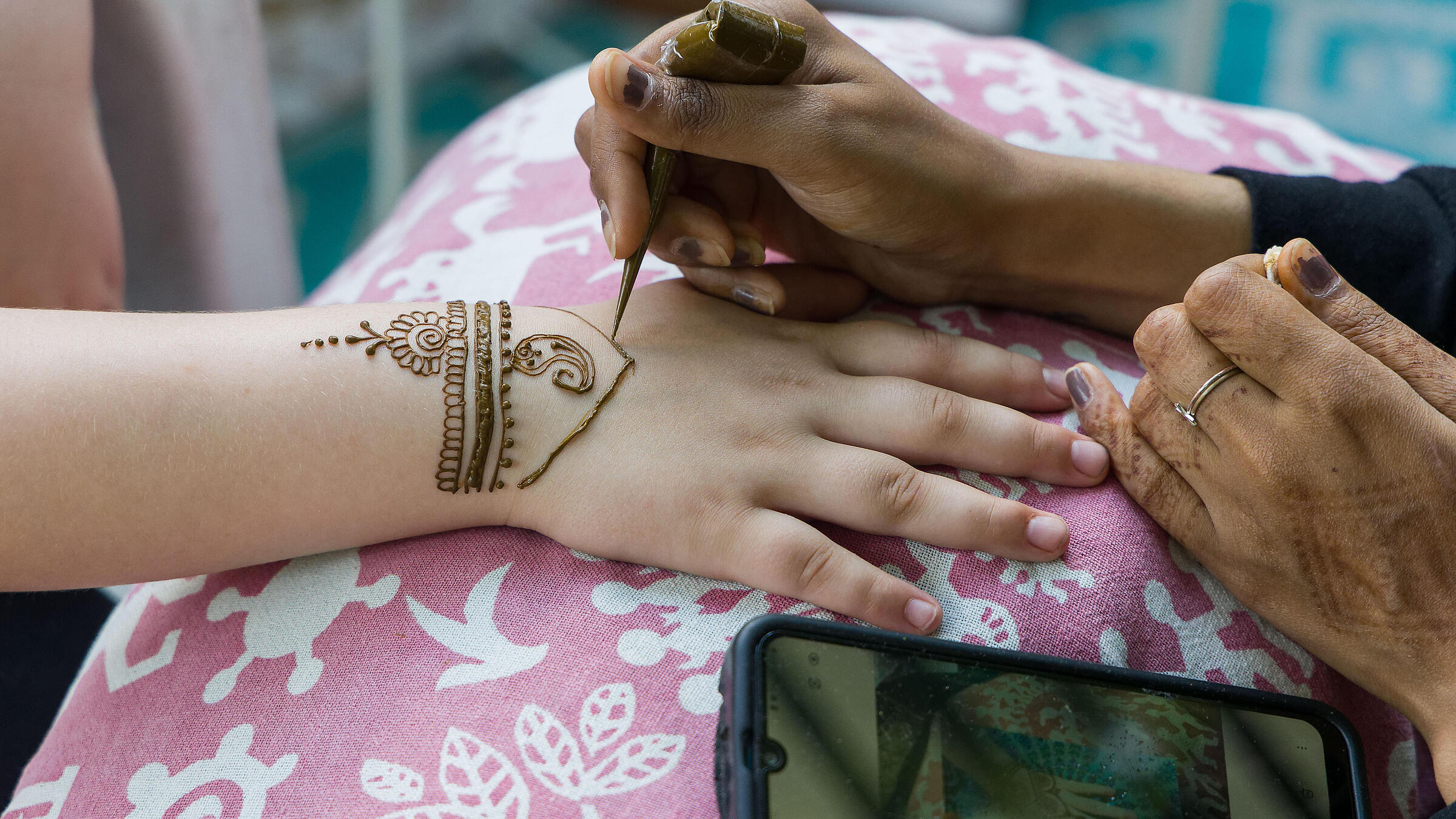 Nahaufnahme zeigt eine Kinderhand, die von einer Künstlerin mit Henna verziert wird.