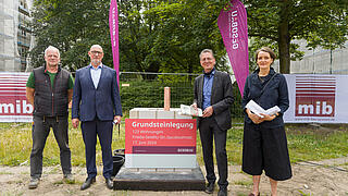 Bild zeigt Grundsteinlegung am Hamburger Platz am 17. Juni 2024 (v.ln.r): Polier Herr Hannemann, Jörg Franzen, Vorstandsvorsitzender der GESOBAU, Christian Gaebler, Seantpr für Stadtentwicklung, Bauen und Wohnen, Julia Dahlhaus, Geschäftsführerin DMSW Architekten. In Mitte Grundstein, im Hintergrund Bestandsgebäude und Bäume.