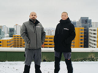 Außenaufnahme zeigt zwei Hausmeister der GEOSBAU auf dem Dach eines Hochhauses im winterlich verschneiten Märkischen Viertel.