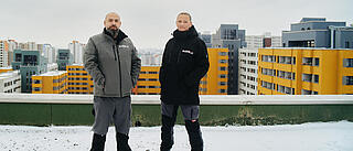 Außenaufnahme zeigt zwei Hausmeister der GEOSBAU auf dem Dach eines Hochhauses im winterlich verschneiten Märkischen Viertel.