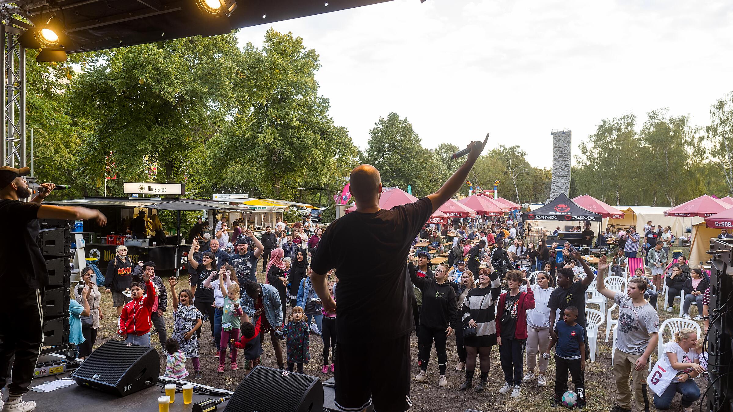 Außenaufnahme zeigt einen Musiker in Aktion auf der Bühne, vor ihm begeisterte Zuhörer*innen.