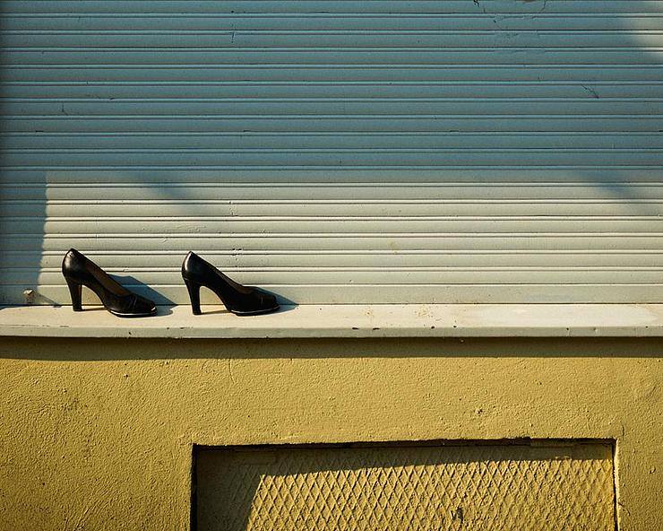 Ein Paar Absatzschuhe steht auf einem Fenstersims vor einer herabgelassenen Jalousie. 
