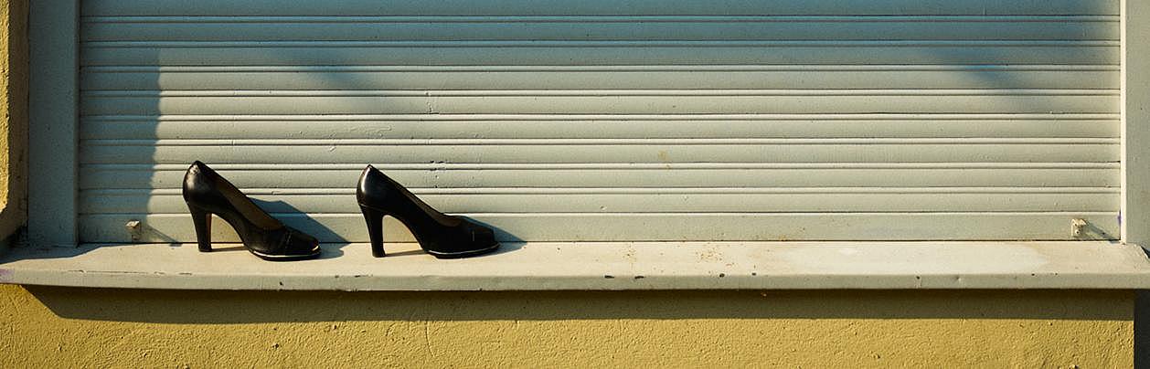 Ein Paar Absatzschuhe steht auf einem Fenstersims vor einer herabgelassenen Jalousie. 