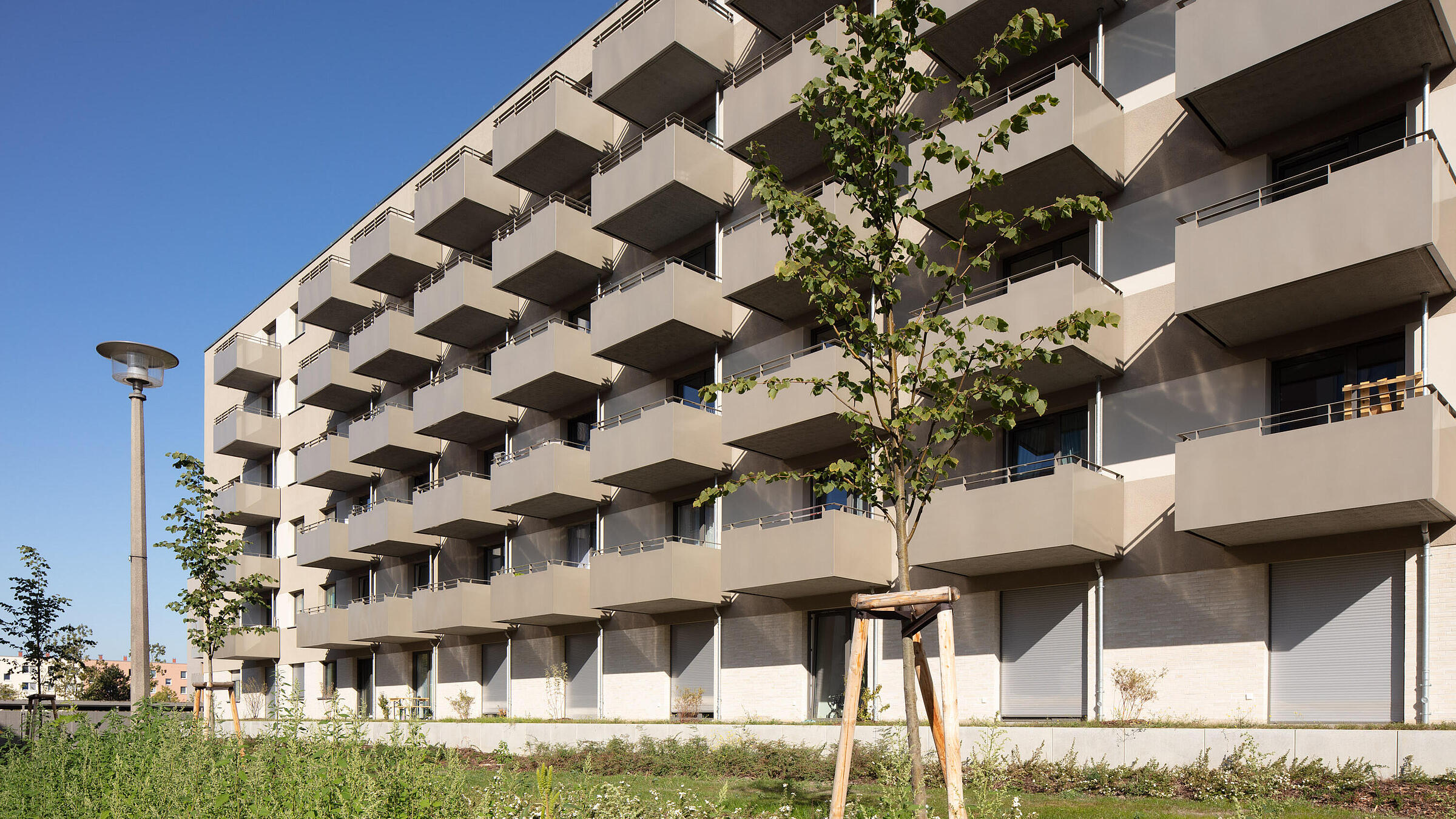 Fünfgeschossiges Wohnhaus mit Balkonen. Im Vordergrund ist eine Grünfläche zu sehen.