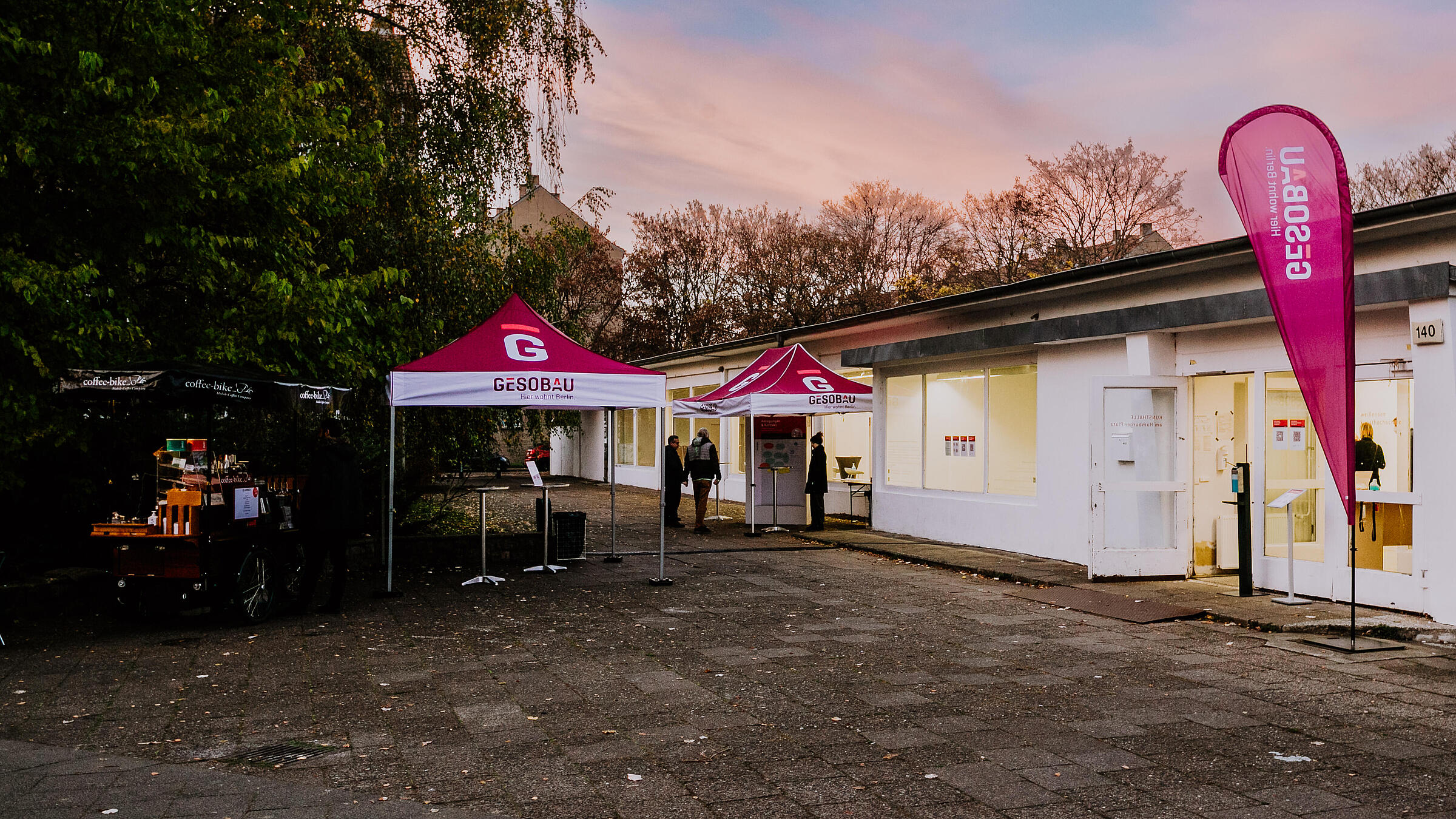 Bild zeigt zwei GESOBAU Pavillons und eine Beachflag vor der erleuchteten Kunsthalle in der Dämmerung.