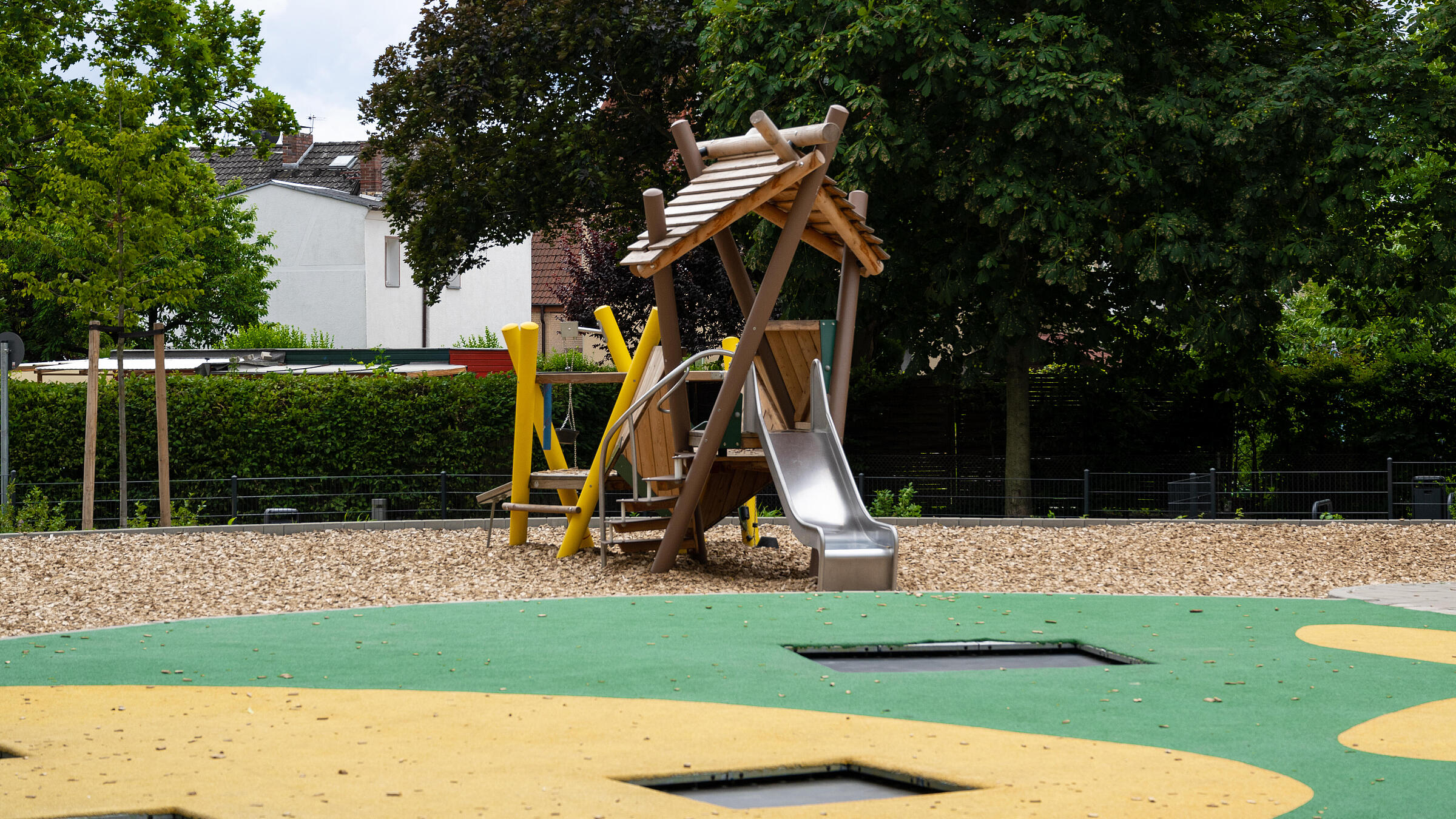 Außenaufnahme der neuen Spielflächen am Wilhelmsruher Damm. Im Vordergrund Bodentrampoline, im Hintergrund Spielgerüst vor Bäumen.