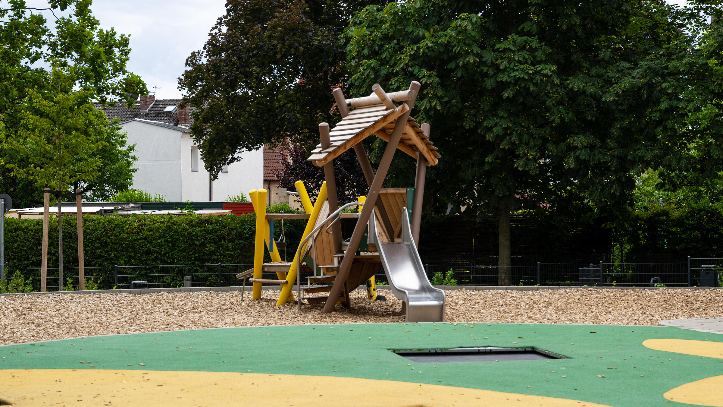 Außenaufnahme der neuen Spielflächen am Wilhelmsruher Damm. Im Vordergrund Bodentrampoline, im Hintergrund Spielgerüst vor Bäumen.