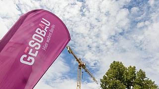 Bildzeigt GESOBAU-Flagge, im Hintergund Baukran, blauer Himmel, Baum.