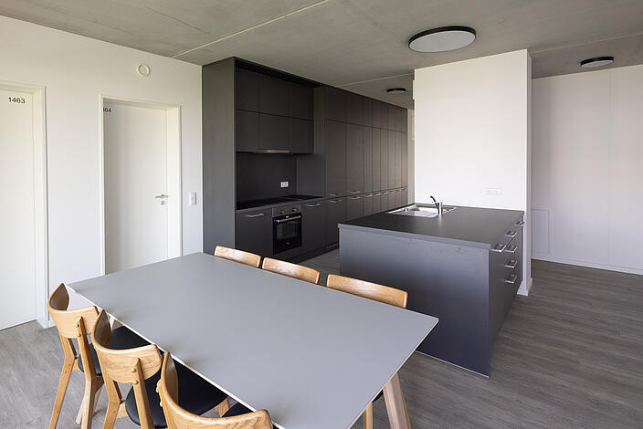 Innenaufnahme zeigt eine Wohnküche mit einem Esstisch für sechs Personen und einer Kochinsel.