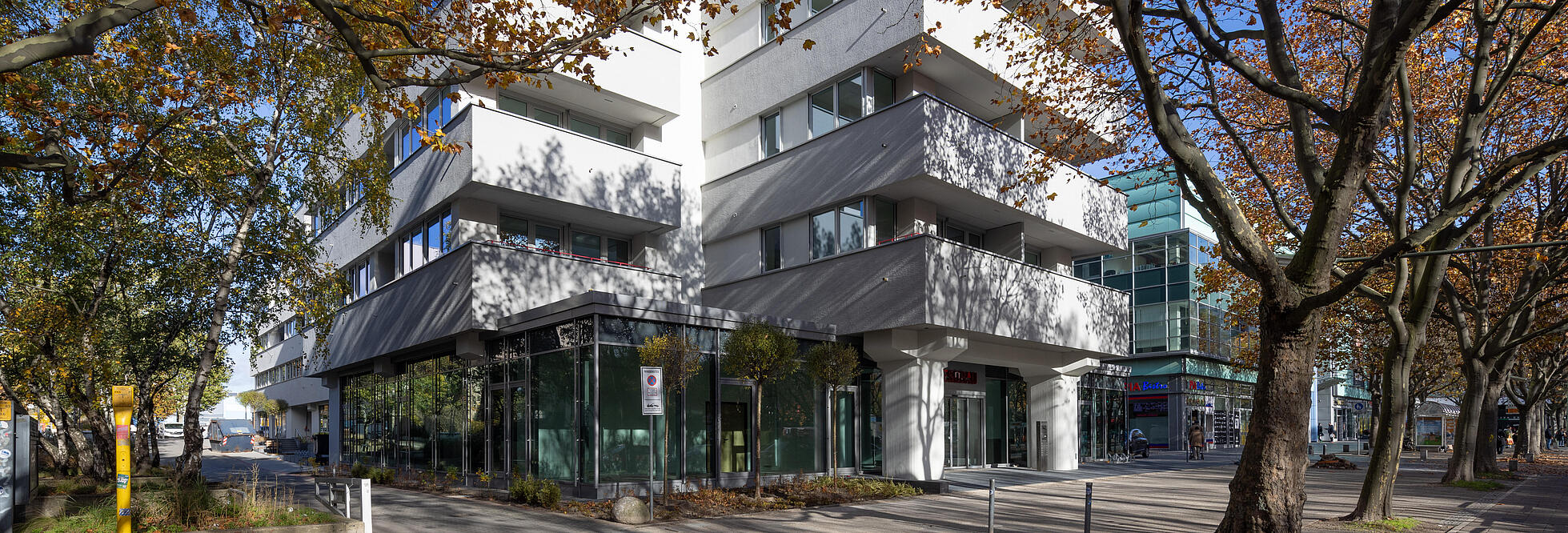 Außenansicht: Neugestaltete Straßenansicht des Wohn- und Geschäftsgebäudes Wilhelmsruher Damm 142. Im Vordergrund herbstliche Bäume