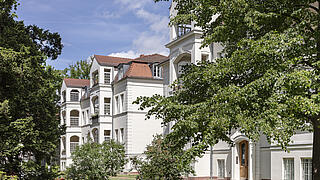 Bild zeigt Häuser der Wohnanlage Amalienpark in Pankow. Im Vordergrund Bäume.