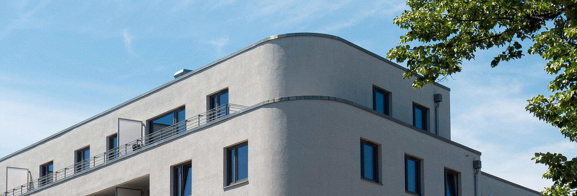 Außenaufnahme zeigt die Fassade des fertigen Wohnhauses mit der markanten abgerundeten Ecke.