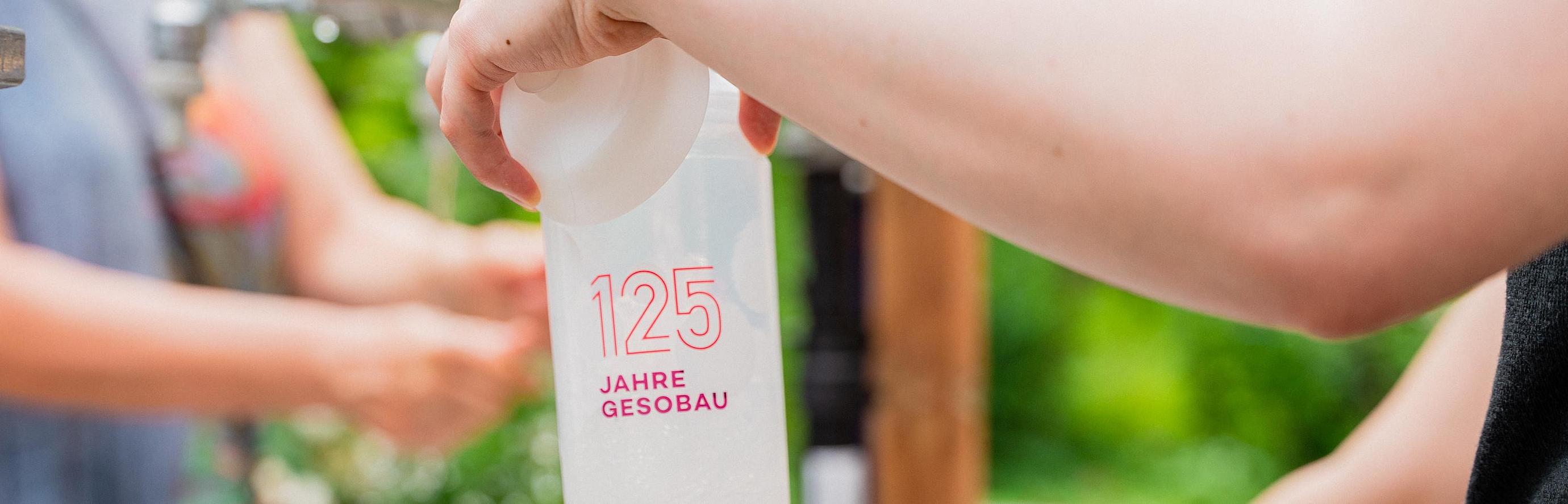 Nahaufnahme einer sich im Auffüllen befindlichen Wasserflasche mit dem GESOBAU Logo darauf.