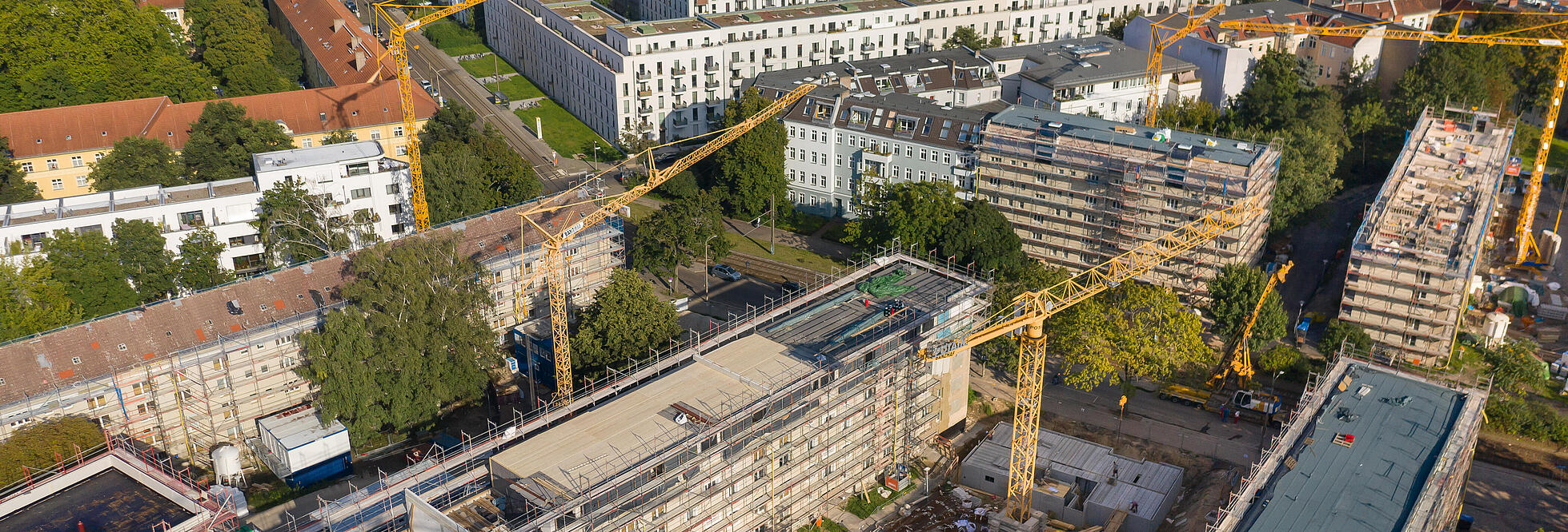 Außenaufnahme zeigt die Gebäude entlang des Stiftswegs aus der Luft, in den Innenhöfen jeweils Baukräne. Alle Häuser sind eingerüstet, mittig ein teilweise abgedecktes Dachgeschoss, das für die Aufstockung vorbereitet wird. 