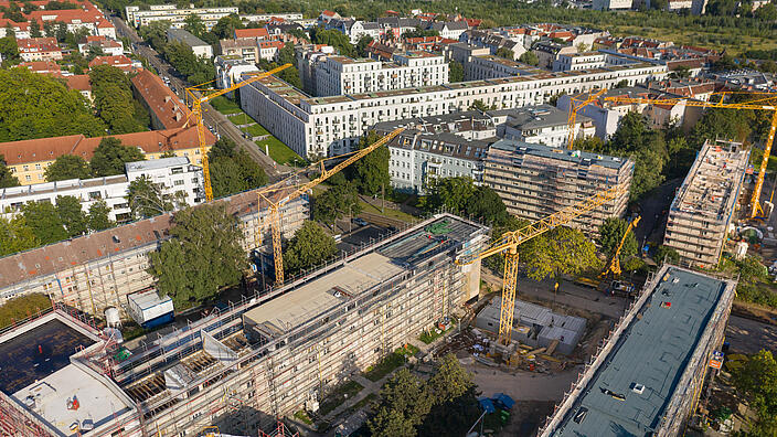 Außenaufnahme zeigt die Gebäude entlang des Stiftswegs aus der Luft, in den Innenhöfen jeweils Baukräne. Alle Häuser sind eingerüstet, mittig ein teilweise abgedecktes Dachgeschoss, das für die Aufstockung vorbereitet wird. 