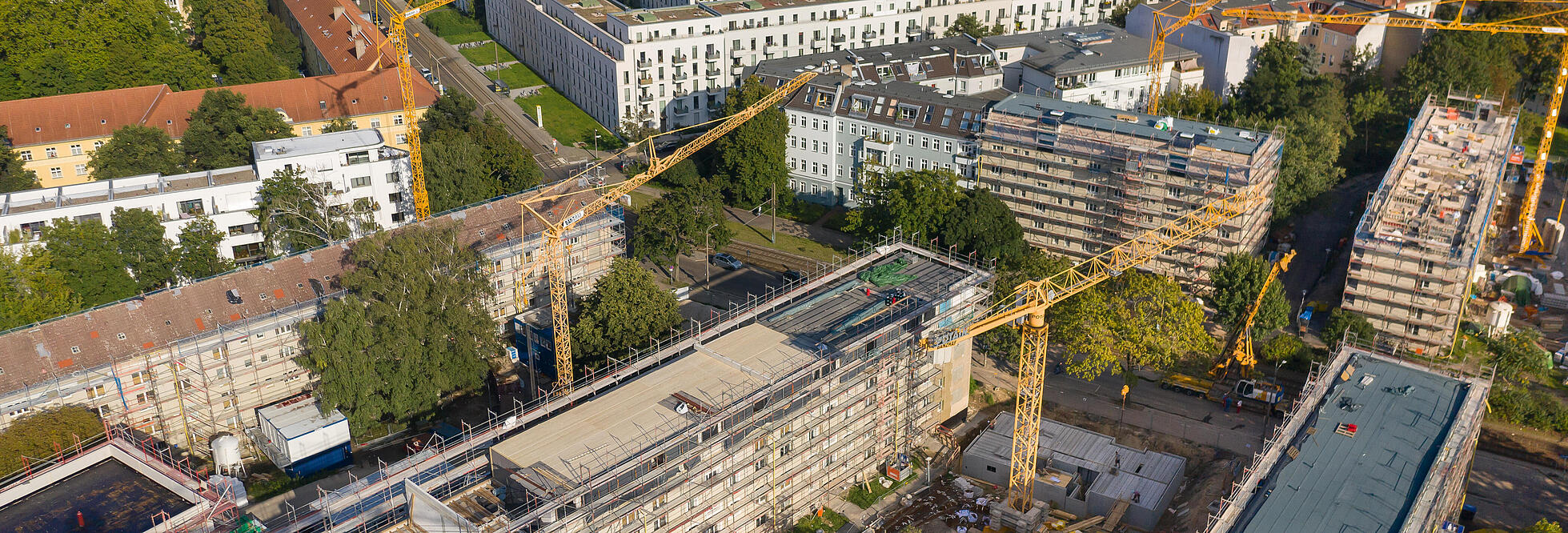 Außenaufnahme zeigt die Gebäude entlang des Stiftswegs aus der Luft, in den Innenhöfen jeweils Baukräne. Alle Häuser sind eingerüstet, mittig ein teilweise abgedecktes Dachgeschoss, das für die Aufstockung vorbereitet wird. 