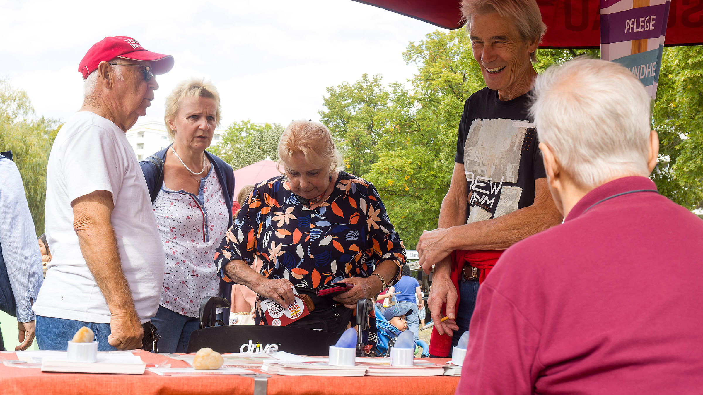 Außenaufnahme zeigt eine Gruppe älterer Besucher*innen vor einem Stand.