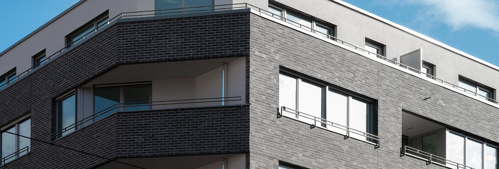 Außenaufnahme zeigt die obere Hälfte der eckigen Fassade der Langhansstraße 28: ein Staffelgeschoss und zwei verklinkerte Etagen mit Balkonen.