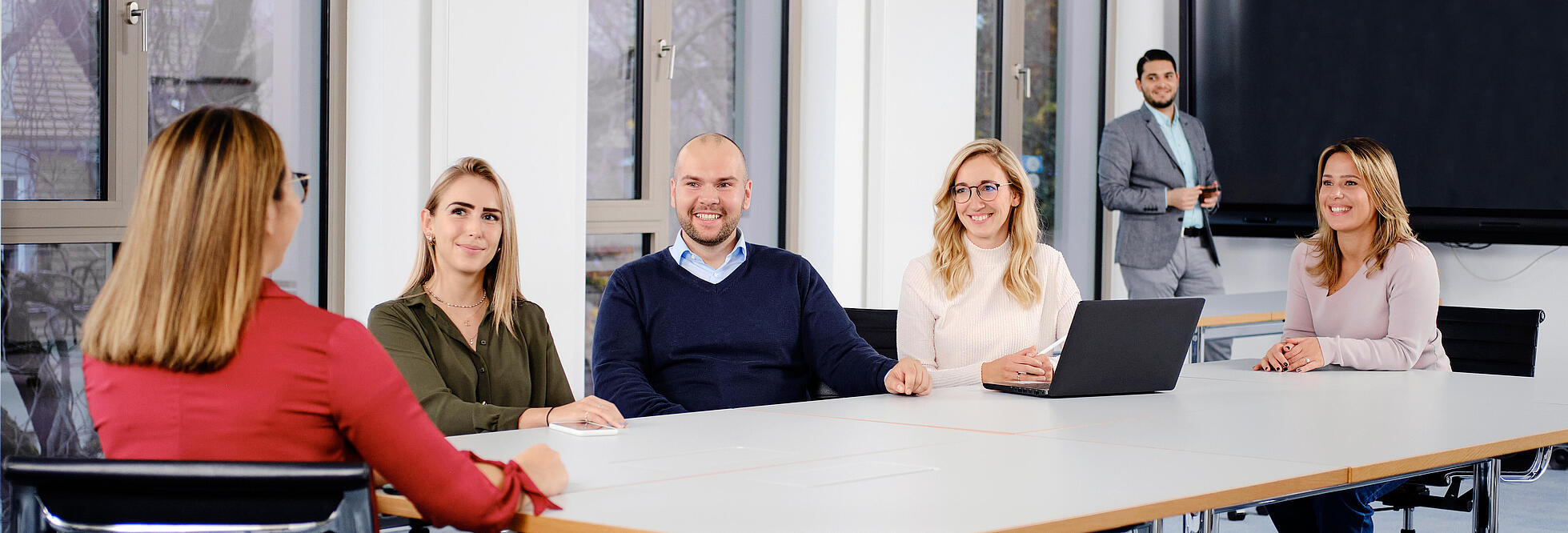 Innenaufnahme zeigt eine Gruppe Mitarbeiter*innen der Gesobau in einem der Konferenzräume am Stiftsweg. Im Hintergrund sichtbar ein Smartboard.