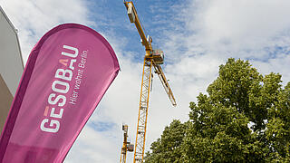 Bild zeigt GESOBAU-Fahne im Wind, im Hintergrund blauer Himmel, Baum und Kran.