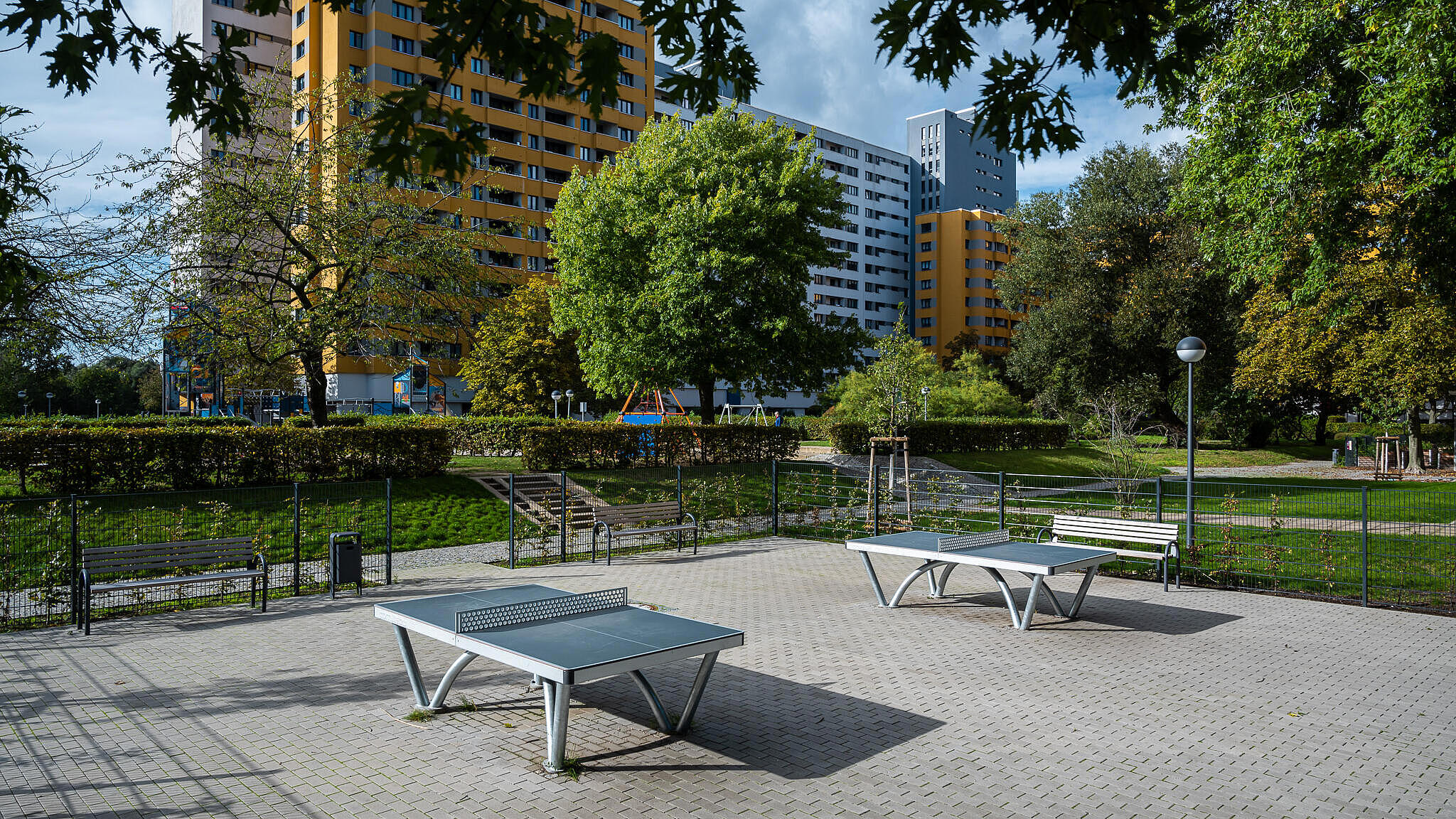Bild zeigt Fläche Außenanlagen mit Tischtennisplatten im Märkischen Viertel. Im Hintergrund Bäume und Wohnhäuser.