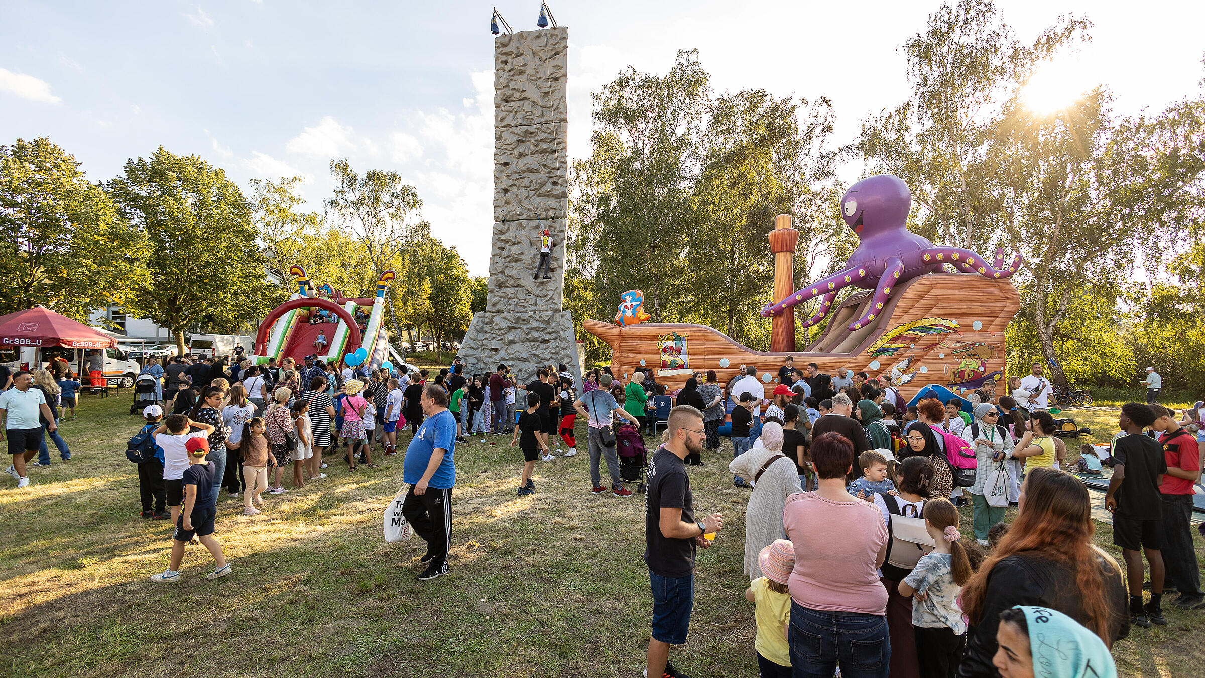Außenaufnahme zeigt den Kinderspielbereich auf dem Begegnungsfest: ein Kletterturm, eine Hüpfburg in Form eines Piratenschiffs und eine aufblasbare Rutsche.
