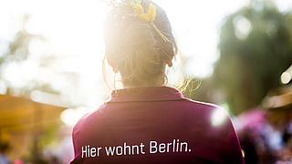 Eine Mitarbeiterin der GESOBAU steht mit dem Rücken zur Kamera, auf ihrem Rücken steht der Slogan "Hierwohnt Berlin."