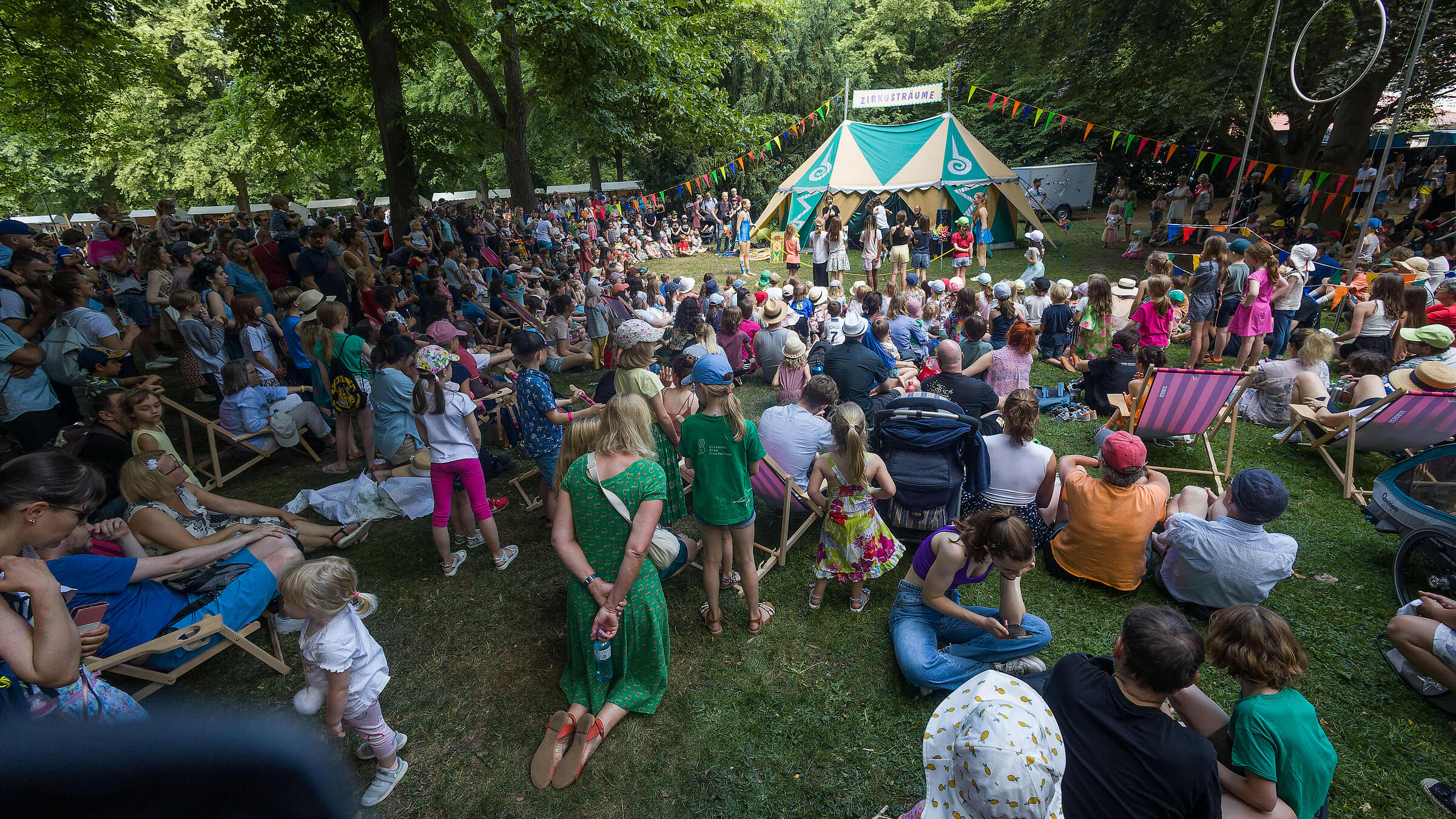 Wiese mit Besucher*innen vor dem Zirkuszelt