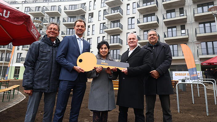 Bild zeigt Schlüsselübergabe in der Titiseestraße am 6. November 2024 (v.l.n.r.): Christian Gaebler (Senator Stadtentwicklung, Bauen und Wohnen), Arjen ten Brinke (Geschäftsführer Ten Brinke), Emine Demirbüken-Wegner (Bezirksbürgermeisterin Reinickendorf), Christian Wilkens (Vorstand GESOBAU) und Thomas Harms (Superintendent Kirchenkreis Reinickendorf). In der Mitte großer Schlüssel. Im Hintergrund Wohngebäude.