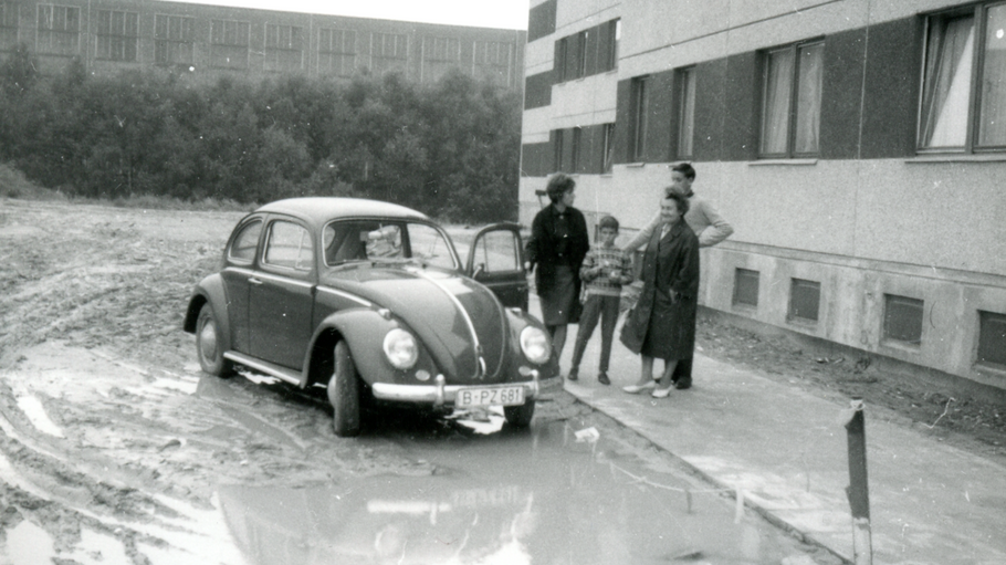 Außenaufnahme zeigt einen VW-Käfer im Matsch vor einem frisch errichteten Neubau im Märkischen Viertel.