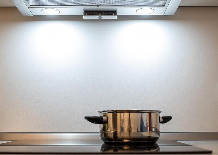 Topf steht auf einer Kochfläche, darüber hängt ein Sensor, der bei möglicher Gefahr Alarm schlägt.