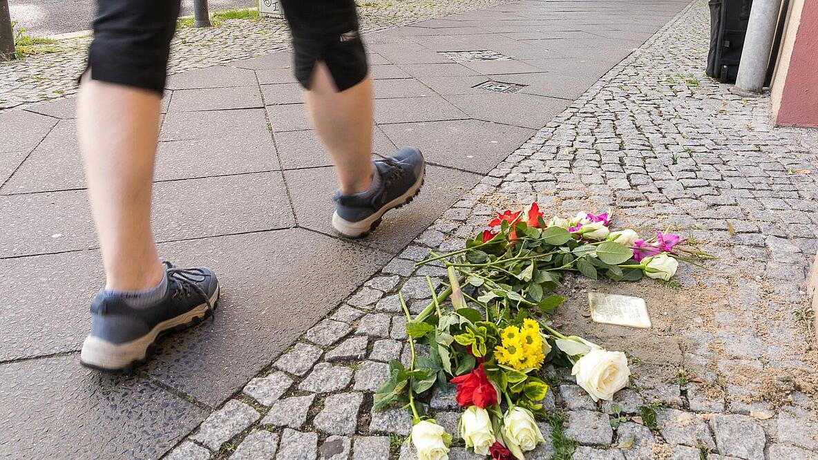 Außenaufnahme zeigt einen frisch gelegten Stolperstein in der Florastraße 36 mit Blumen darvor.