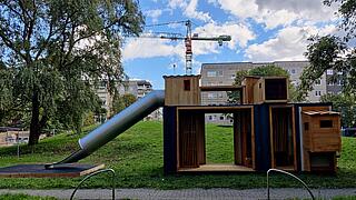 Außenaufnahme zeigt einen hölzernen Spielcontainer mit Tunnelrutsche und verschiedenen Versteckmöglichkeiten.