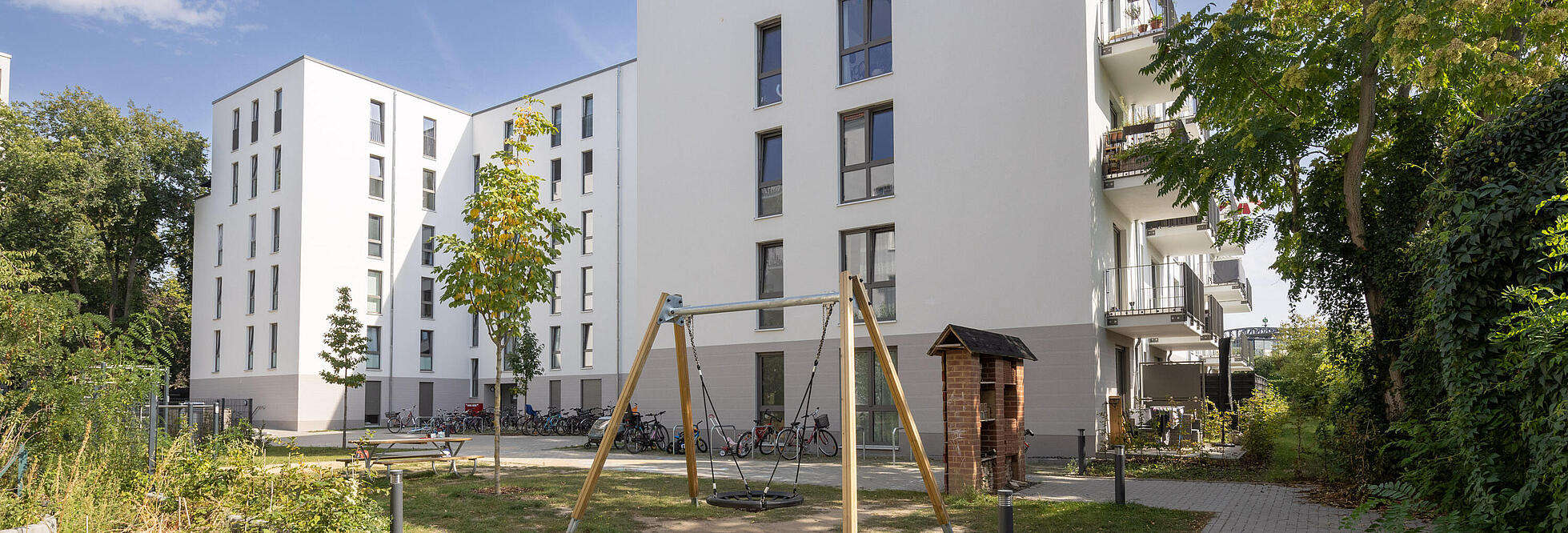 Bild zeigt Außenaufnahme des fertiggestellten Wohnhauses in der Grüntaler Straße 50 a, b (September 2023), Im Vordergrund Spielbereich für Kinder und Grünflächen.