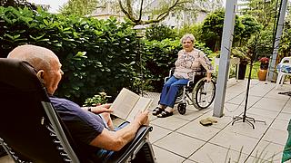 Außenaufnahme: Mann in Gartenstuhl und Frau in Rollstuhl auf Terrasse